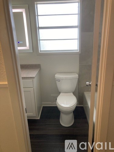 A white toilet in a small bathroom with a window above it.