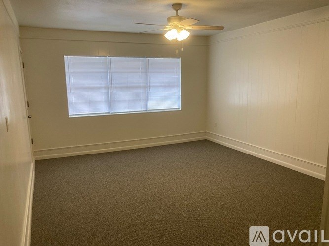 A room with a carpeted floor, a ceiling fan, and a window with blinds.