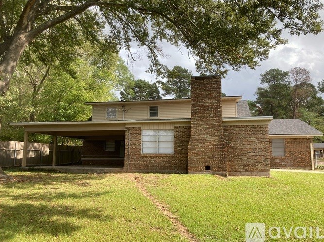 A house with a brick chimney is surrounded by green grass and trees.