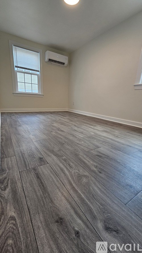 A room with wooden flooring and a window with an air conditioner.