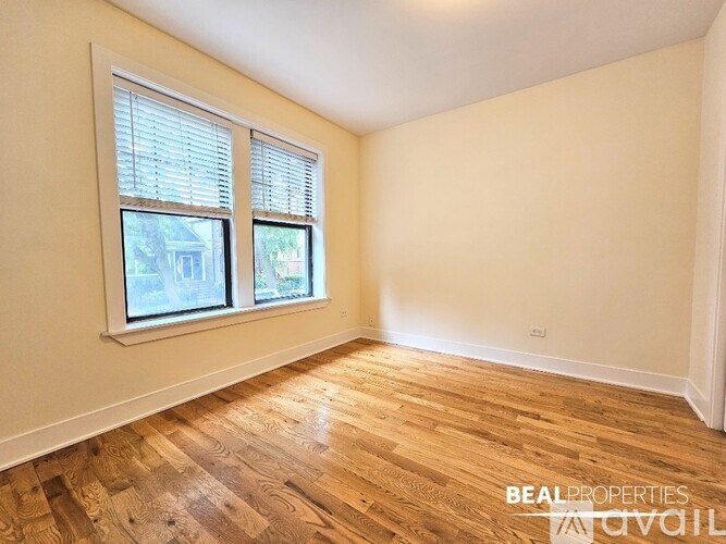 A room with wooden flooring and a window showing a view of a house.