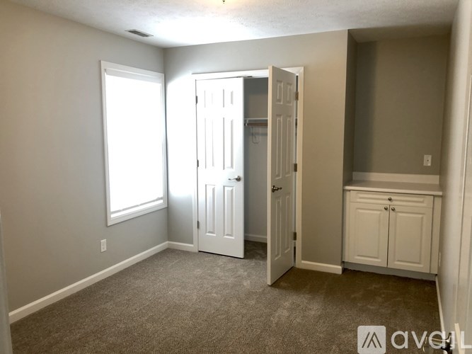 A room with a carpeted floor, a window, and a door leading to another room.