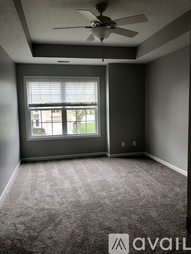 A room with a carpeted floor, a ceiling fan, and a window with blinds.