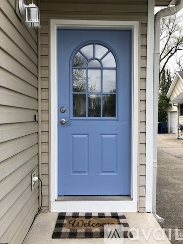 A blue door with a glass window and a black and white mat on the porch.