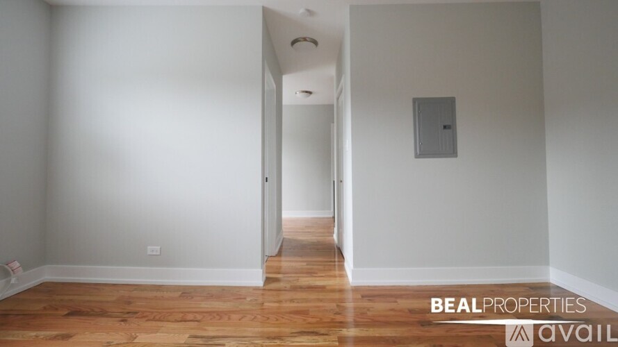 A room with wooden floors and white walls, with a doorway leading to another room.
