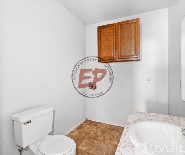 A white toilet sits in a bathroom with a wooden cabinet and a round logo on the wall.