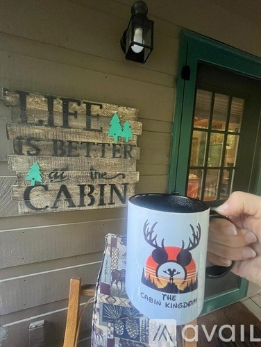 A mug with a deer head on it is in front of a sign that says "Life is better at the cabin".