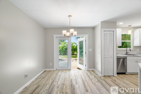 A spacious room with wooden floors and a large window leading to a backyard.