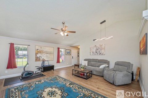 A living room with a rug, a couch, a chair, and a fan.
