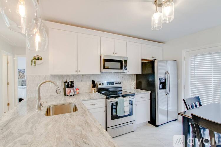 A kitchen with white cabinets and appliances, a sink, and a dining table.