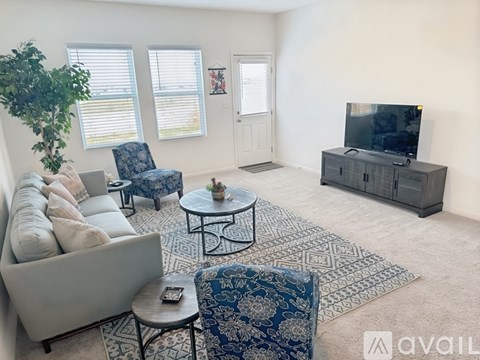 A living room with a grey couch, a blue patterned chair, a black coffee table, and a television on a cabinet.