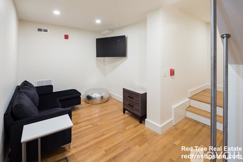 A living room with a black couch, a television, and a wooden floor.