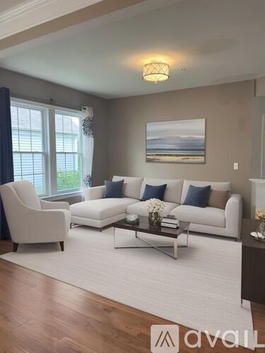 A living room with a white couch, a chair, and a painting on the wall.