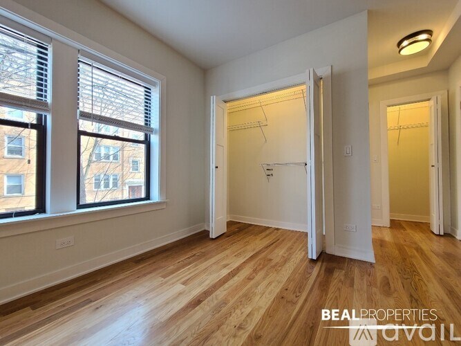 A room with wooden floors and white walls, with a large window on the left and a closet with a white door on the right.