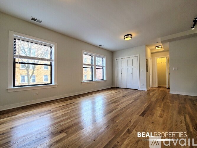A spacious room with wooden floors and two windows.