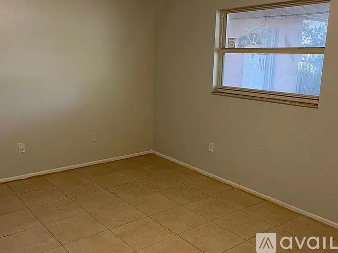 A room with beige tiled flooring and a window showing a view of a building outside.