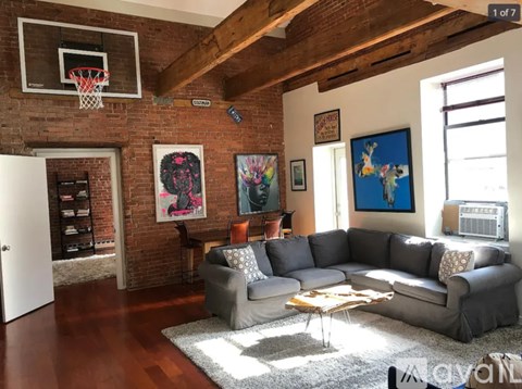 A living room with a grey couch and a basketball hoop on the wall.