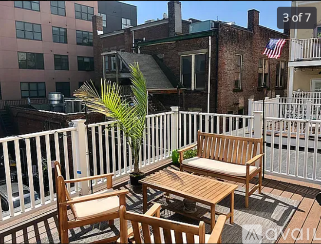 A patio with a white railing, wooden furniture, and a palm tree.