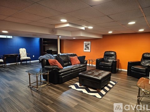 A living room with black leather furniture and orange walls.