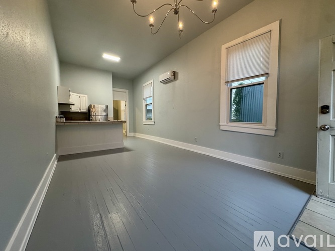 A spacious room with a chandelier, a window with blinds, and a door on the right.