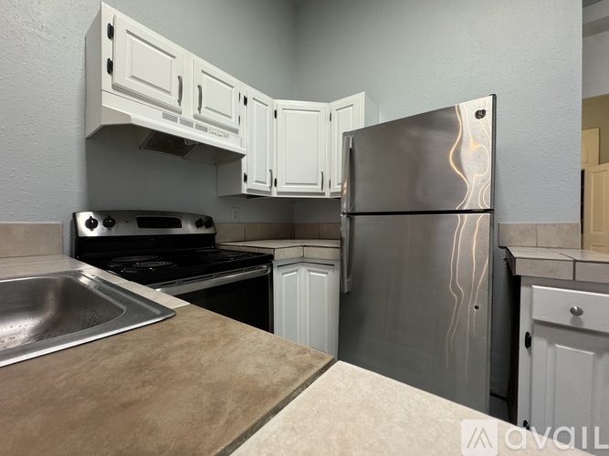 A kitchen with a stainless steel refrigerator, a stove, and white cabinets.