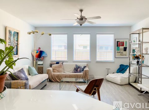 A living room with a white couch, a glass table, and a ceiling fan.
