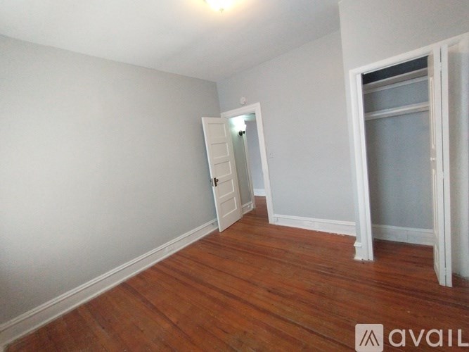 A room with wooden floors and white walls, with a doorway leading to another room.