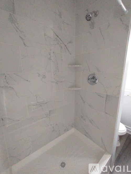 A white marble tiled shower with a drain in the middle.