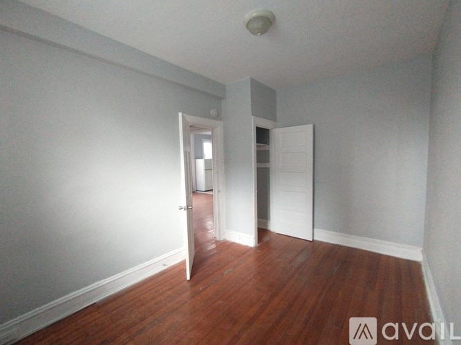 A room with wooden floors and white walls with a door open to another room.