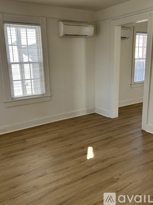 A room with wooden flooring and two windows.