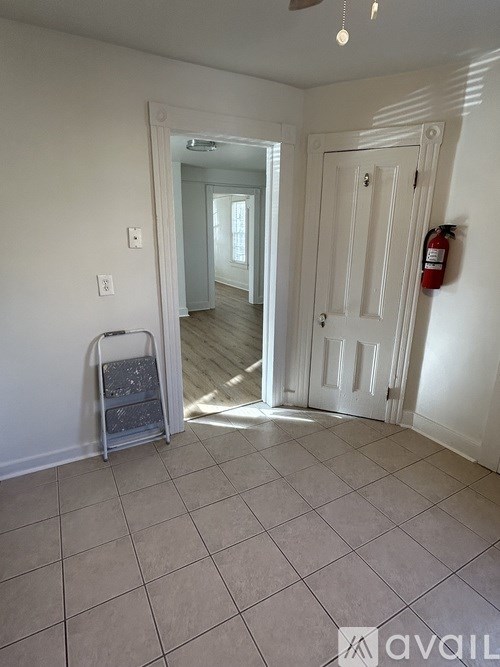 A room with a white door, a fire extinguisher on the wall, and a tiled floor.