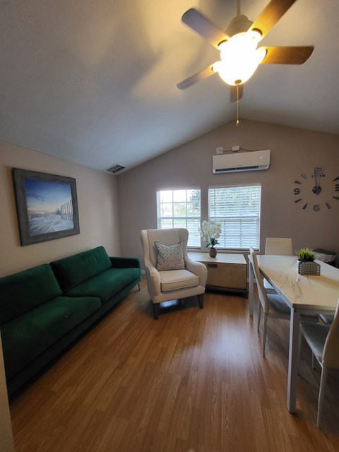 A living room with a green couch, a white chair, and a wooden floor.