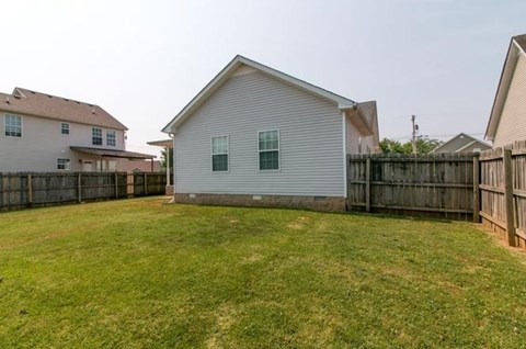 A small white house with a green window is surrounded by a fence and a grassy yard.