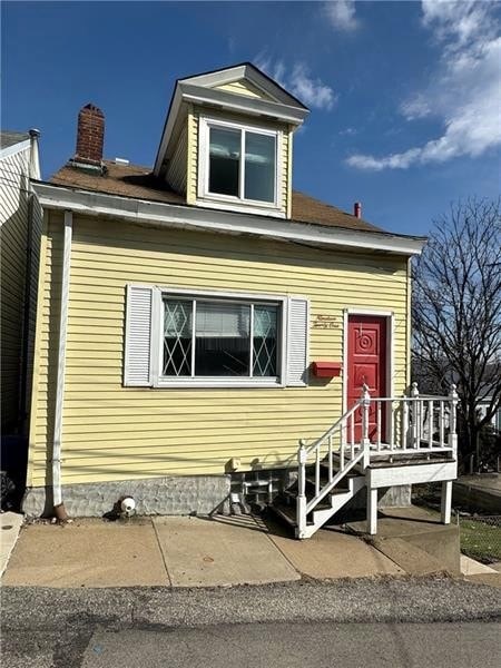 A yellow house with a red door and a small porch.