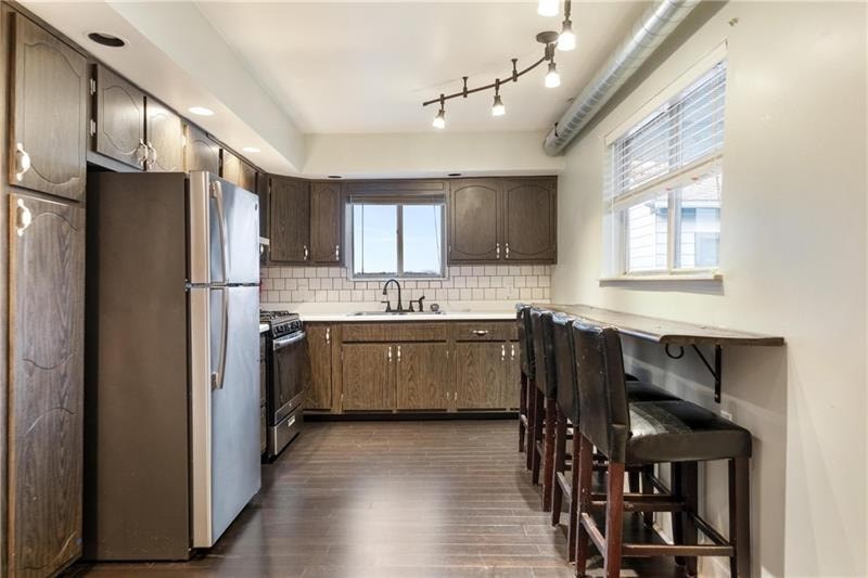 A kitchen with a refrigerator, stove, and bar stools.