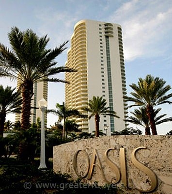 A tall white building with the word Oasis written on a stone wall in front of it.
