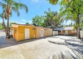 A yellow house with a white door is surrounded by palm trees.