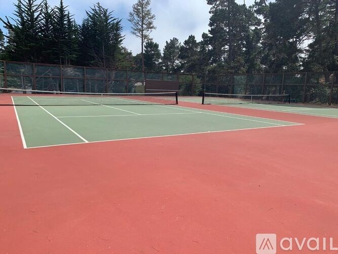 A tennis court with a red surface and green boundary lines.
