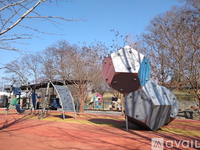 A playground with a large grey and red structure in the foreground and a slide in the background.