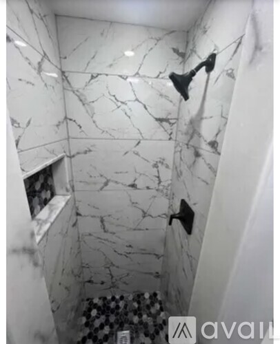 A white marble bathroom with a black shower head.
