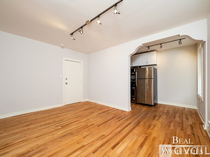 A spacious room with wooden flooring and a stainless steel refrigerator.