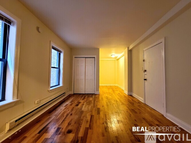 A room with wooden floors and white walls, with a window on the left and a door on the right.