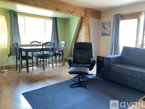 A living room with a grey couch, a black chair, and a dining table with chairs.
