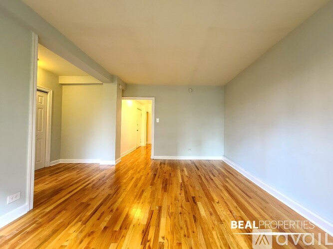 A room with wooden floors and white walls, with a door on the left and a window on the right.