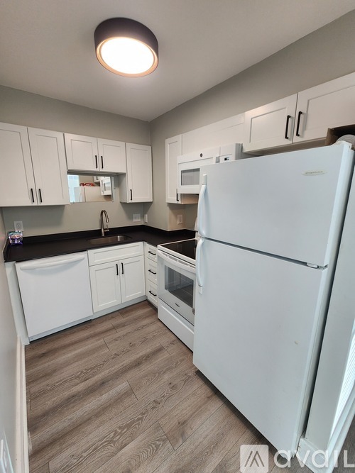 A white refrigerator stands in a kitchen with white cabinets and a wooden floor.