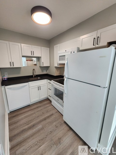 A white refrigerator stands in a kitchen with white cabinets and a wooden floor.