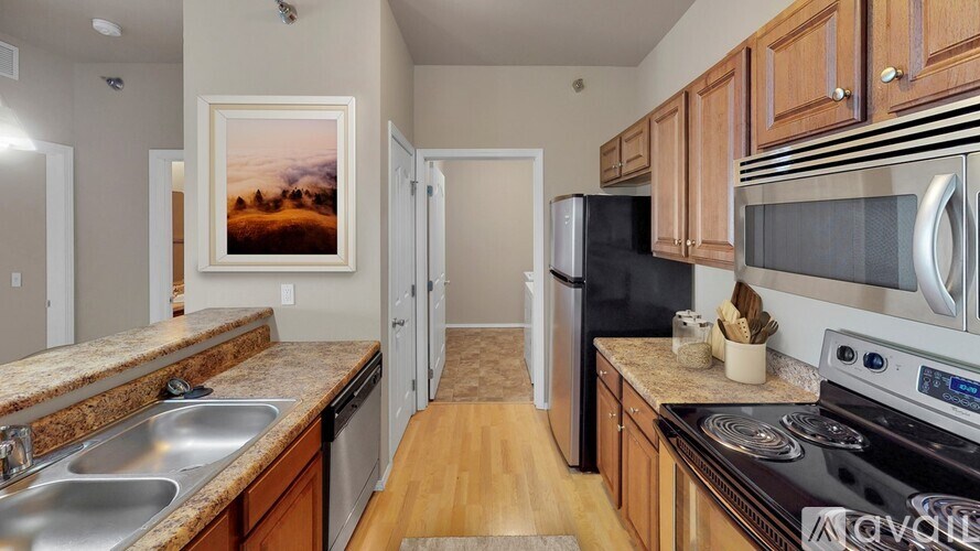 A kitchen with wooden cabinets and a painting of a sunset on the wall.