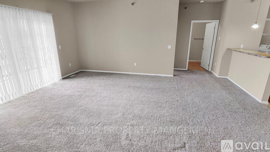 A sparsely furnished room with a carpeted floor and a window with blinds.