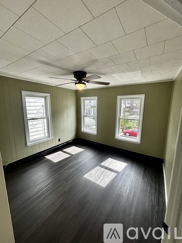 A room with a ceiling fan and three windows.