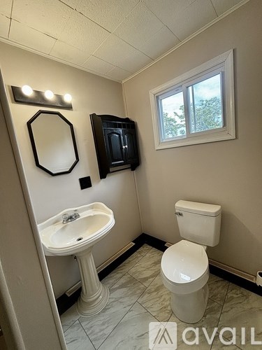 A bathroom with a toilet, sink, mirror and window.